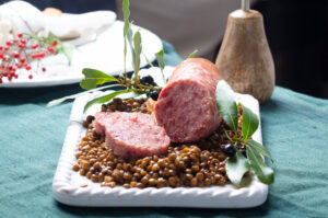 Italian large pork sausage cotechino served  with lentils on white plate.